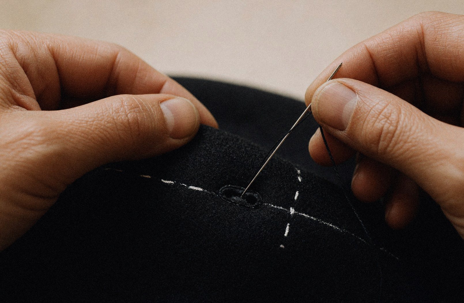 A buttonhole being sewn by hand in dark cloth