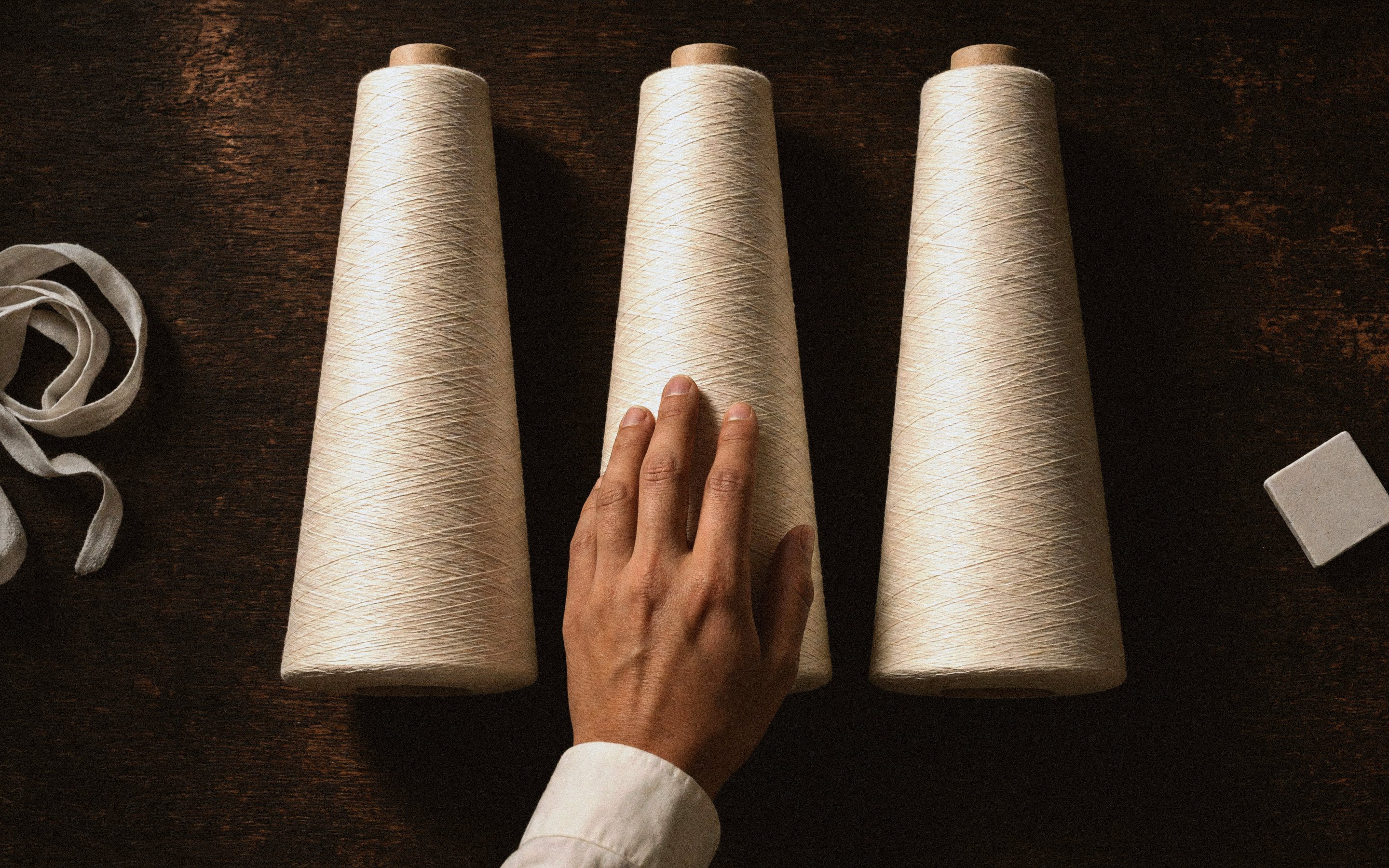 Cones of white thread, a tape measure and chalk under the tailor's hand