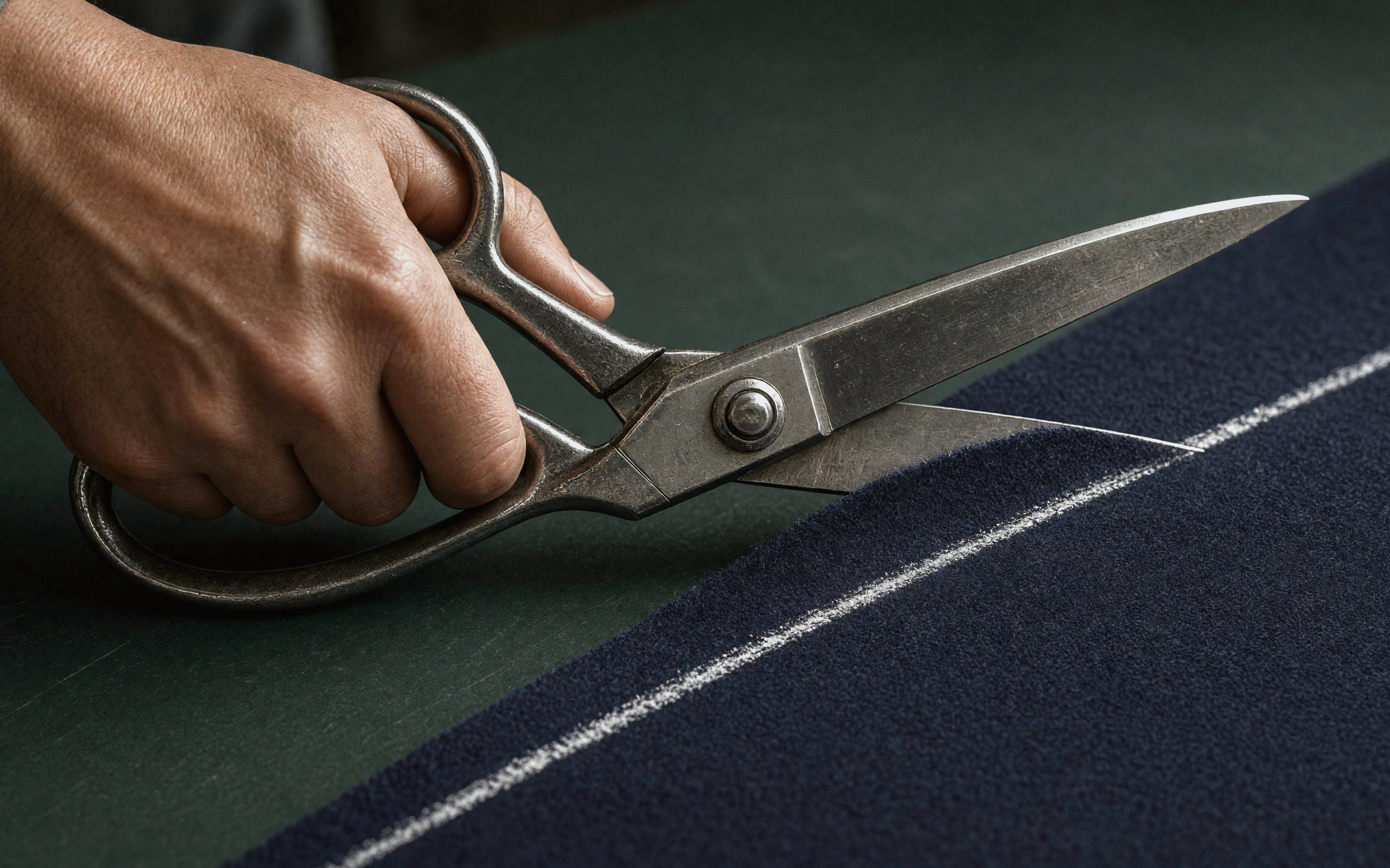 Tailor's shears cutting navy cloth along a chalk line
